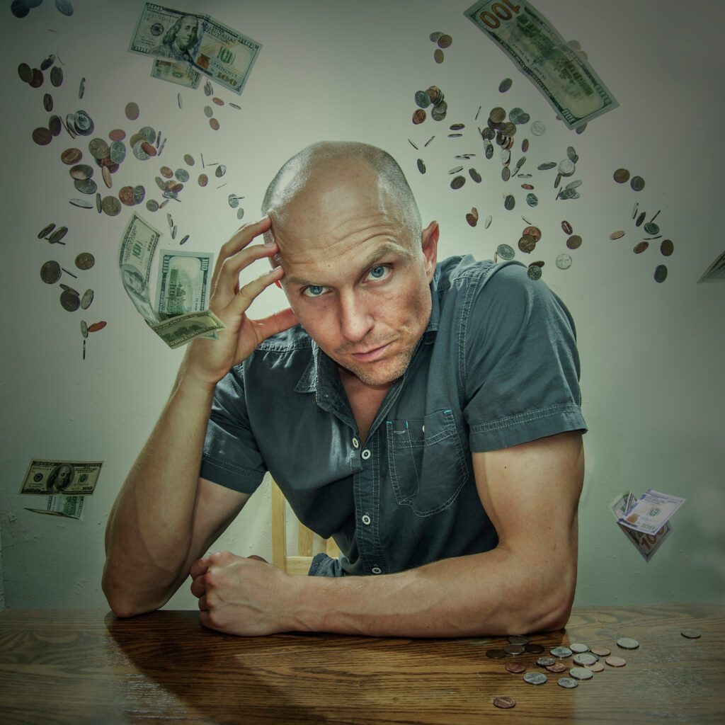 Save Money bald-man-in-grey-polo-holding-forehead-and-leaning-forward-on-table-with-cash-and-coin-money-digital-background